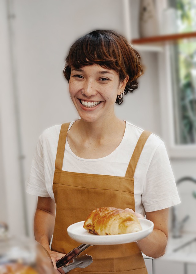 Cajera soteniendo un croissant en un plato blanco con un delantal naranja remera blanca