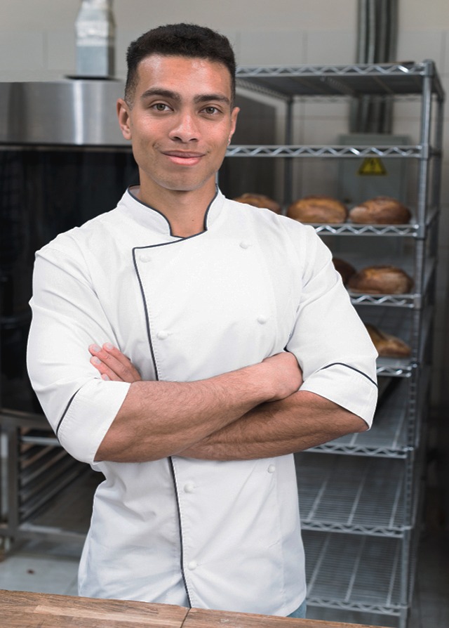 Ayudante del panadero con el mismo traje de chef blanco y con los brazos cruzados