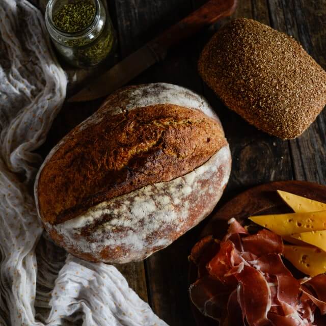 Dos panes caseros, uno de cortaza dura y otro de centeno junto a fetas de jamón crudo y queso