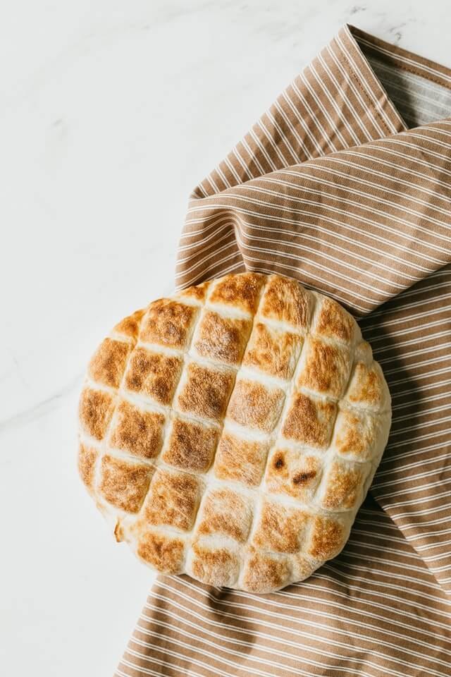 Pan árabe tostada sobre un repasador marrón con rayas blancas en una mesada de mármol blanca grisácea