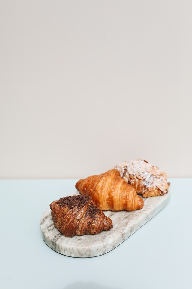 Tres tipos de croissant sobre una bandeja de marmol gris en una mesa de color celeste claro